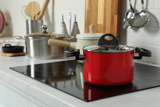 Red pot on electric stove in kitchen. Cooking utensil - Zdjęcie, obraz