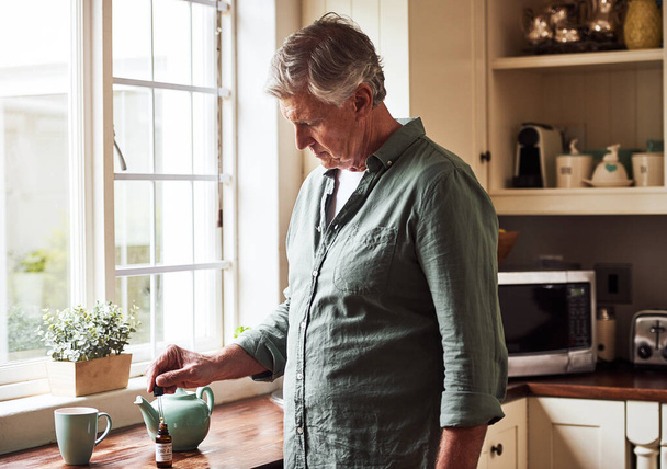 Just a little drop. Cropped shot of a relaxed senior man preparing a cup of tea with CBD oil inside of it at home during the day. - Foto, Bild