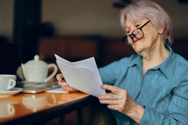 Старшая женщина в очках сидит за столом перед ноутбуком фрилансер работает без изменений - Фото, изображение