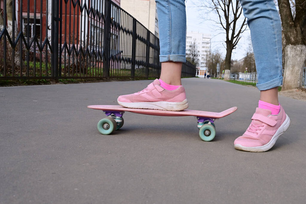 青いジーンズとピンクのスニーカーで女の子のスケートボーダーのクローズアップ足、ピンクのペニースケートロングボードに乗って。国際スケートボードの日。選択的焦点 - 写真・画像