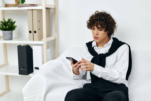 cara encaracolado sentado em um sofá branco smartphone Lifestyle tecnologia - Foto, Imagem