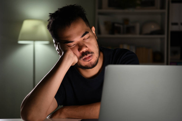 Sobretrabajado cansado, hombre de negocios asiático durmiendo mientras usa la computadora trabajando hasta tarde en la noche en casa - Foto, imagen