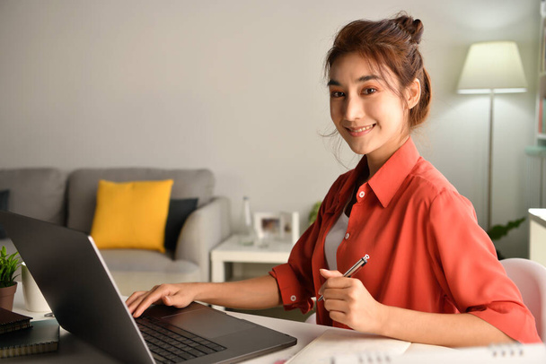 Young Asian businesswoman sitting at home working on laptop computer. Asian woman studying online using laptop surfing information or shopping in internet store - Photo, Image