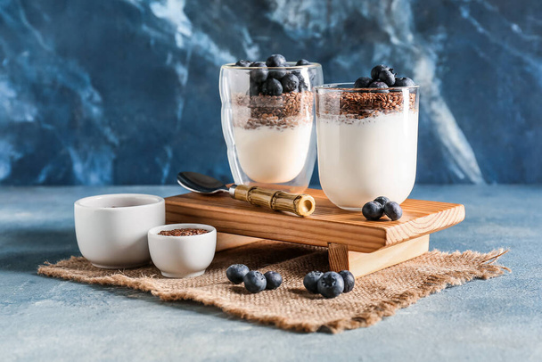 Gläser mit süßem Joghurt, Leinsamen und Blaubeeren auf farbigem Hintergrund - Foto, Bild
