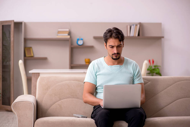 Jeune homme assis sur le canapé avec ordinateur à la maison - Photo, image