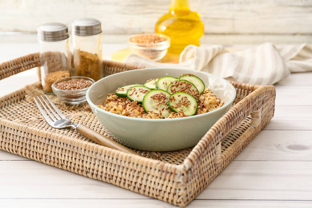 Bowl with tasty oatmeal, flax seeds and cucumber on tray - Photo, Image