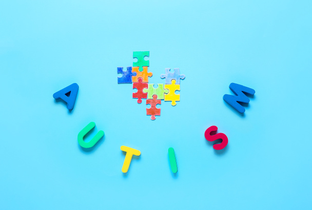 Word AUTISM with colorful puzzle pieces on color background - Photo, Image