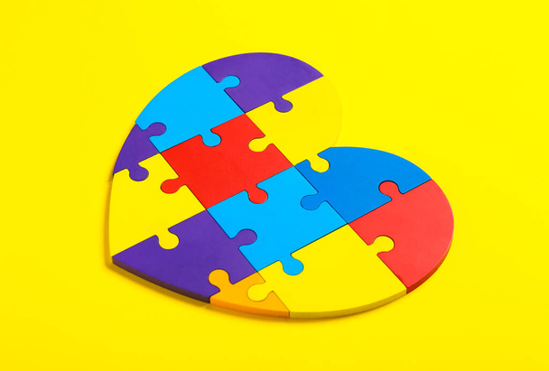 Красочные кусочки головоломки в форме сердца на цветном фоне. Концепция аутистического расстройства - Фото, изображение