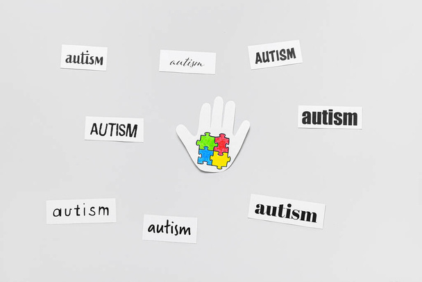 Paper human palm with colorful puzzle pieces and words AUTISM on light background - Foto, afbeelding