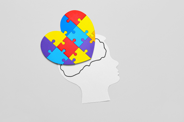 Papier menselijk hoofd met kleurrijke puzzelstukjes in de vorm van het hart op lichte achtergrond. Begrip autistische stoornis - Foto, afbeelding