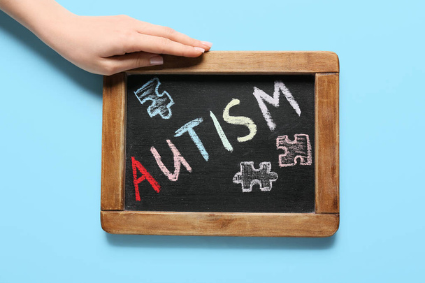 Female hand with word AUTISM written on chalkboard against color background - 写真・画像