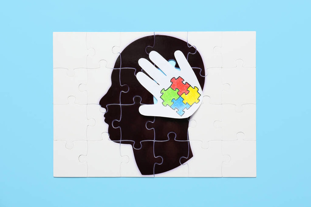 Puzzel met getekend menselijk hoofd en papieren palm met kleurrijke puzzelstukjes op kleur achtergrond. Begrip autistische stoornis - Foto, afbeelding