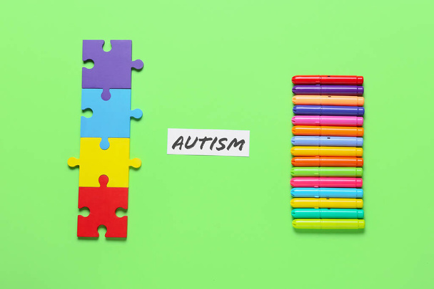 Colorful puzzle pieces and markers with word AUTISM on color background - Photo, Image