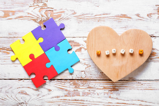 Heart with word AUTISM and colorful puzzle pieces on white wooden background - Photo, Image
