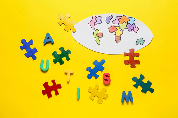 Gezeichnete Weltkarte und bunte Puzzleteile mit Wort AUTISMUS auf farbigem Hintergrund - Foto, Bild