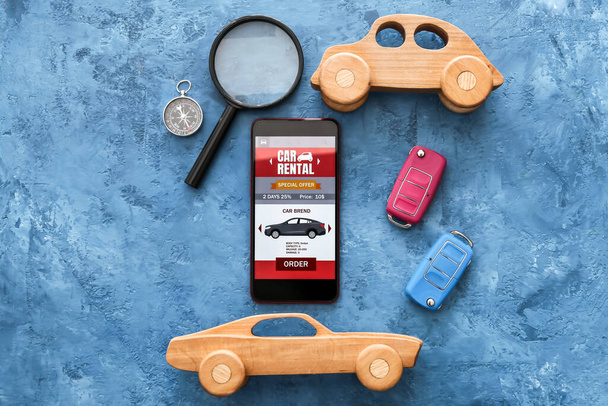 Mobilní telefon s otevřenou půjčovnu aut app, hračky, klíče, lupa a kompas na grunge pozadí - Fotografie, Obrázek