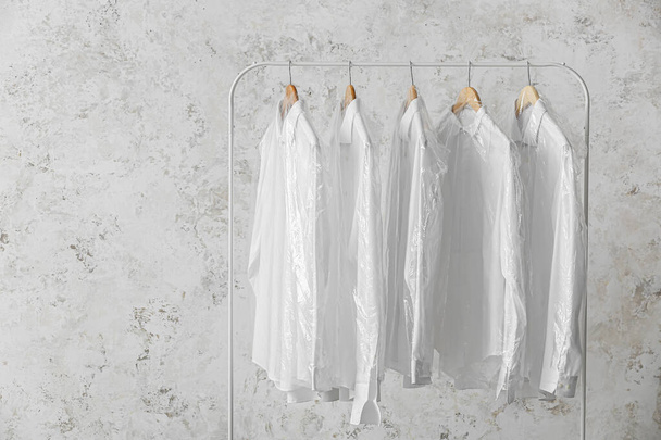Rack with clean white shirts in plastic bags on grunge background - Photo, Image