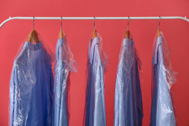 Regal mit sauberen blauen Hemden in Plastiktüten auf rosa Hintergrund - Foto, Bild