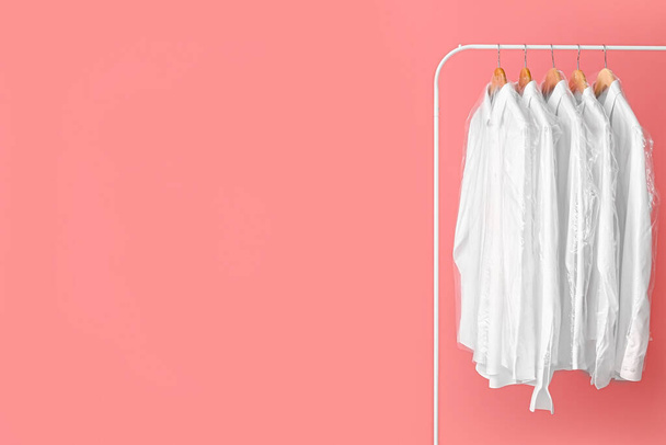 Rack with clean white shirts in plastic bags on pink background - Photo, Image