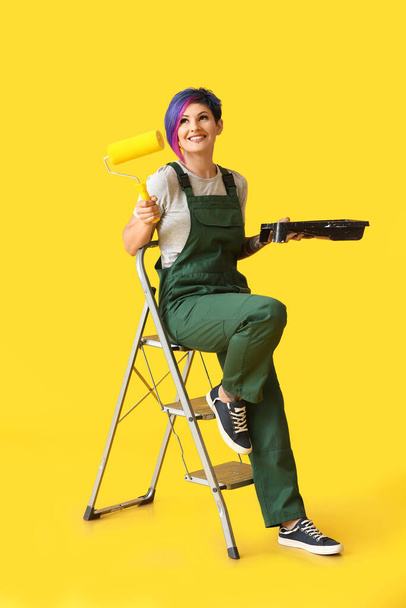 Female painter with paint roller and ladder on yellow background - Photo, Image