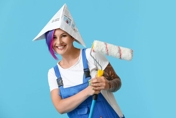 Female painter with paper hat and paint roller on blue background - Photo, Image