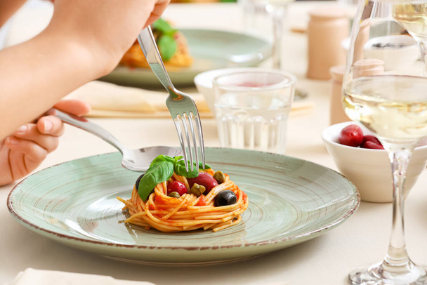 Vrouw eet heerlijke Pasta Puttanesca aan tafel in restaurant - Foto, afbeelding