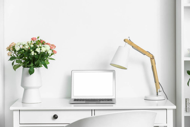 Ваза с букетом красивых свежих роз и современным ноутбуком на столе в номере - Фото, изображение
