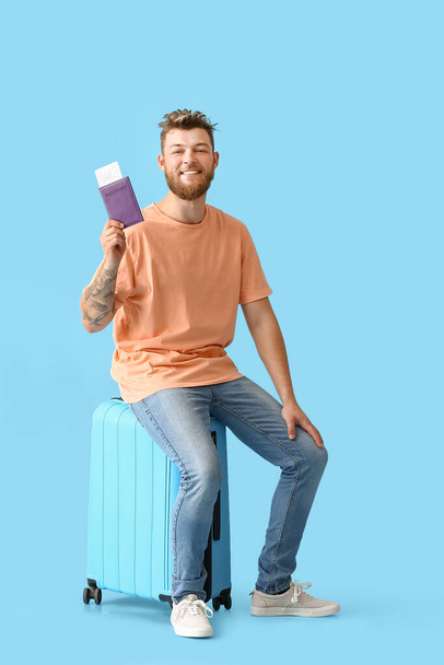 Handsome man with passport and suitcase on blue background - Photo, image