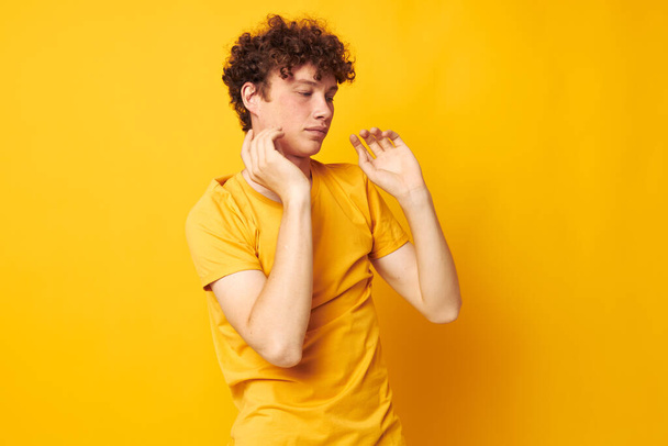 Young curly-haired man yellow t-shirt fashion hand gestures isolated background unaltered - Fotó, kép