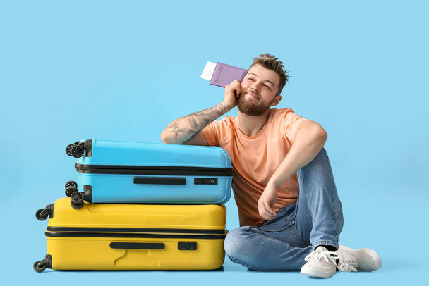 Happy young man with passport and suitcases on blue background - Fotoğraf, Görsel