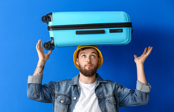 Handsome young man with suitcase on blue background - Φωτογραφία, εικόνα