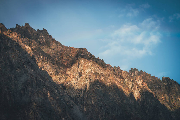 Γραφικό ορεινό τοπίο με μεγάλους βράχους στο χρυσό φως του ήλιου. Φοβερός βραχώδης τοίχος με αιχμηρή κορυφή σε χρυσό ήλιο. Πολύχρωμο ηλιόλουστο τοπίο με ψηλό βραχώδες βουνό με αιχμηρή κορυφή. Ορεινοί τοίχοι. - Φωτογραφία, εικόνα