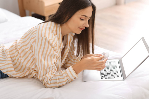 Ładna młoda kobieta z laptopem i słuchawkami w sypialni - Zdjęcie, obraz