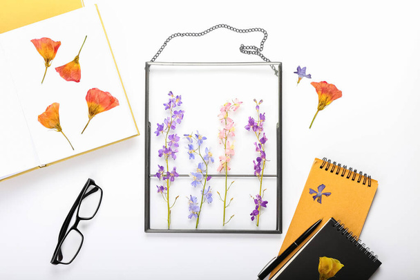 Composición con flores prensadas secas, libro, cuaderno y anteojos sobre fondo blanco - Foto, imagen