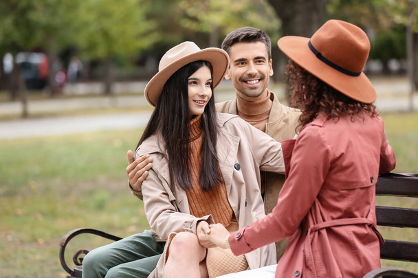Man and two beautiful women sitting on bench in park. Polyamory concept - Fotó, kép