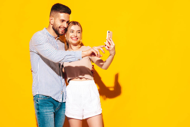 Sexy smiling beautiful woman and her handsome boyfriend. Happy cheerful family having tender moments near yellow wall in studio.Looking at cellphone screen. Using smartphone apps - Photo, Image