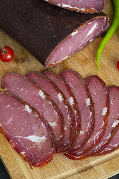 Turkish pastrami on a wooden serving plate. Whole and sliced pastrami. pastrami is made from the ribeye and beef fillet parts of the cow. Close up. - Photo, Image