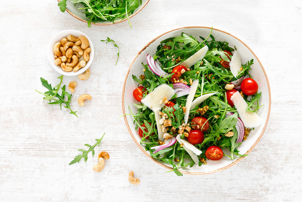 Fresh vegetable salad with arugula, tomato, onion, parmesan cheese and cashew nuts. Top view - Fotoğraf, Görsel