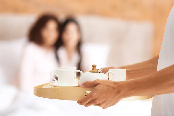Man with breakfast for two beautiful women in bedroom. Polyamory concept - 写真・画像