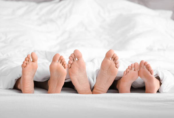 Piedi di uomo e due donne sdraiate sotto una coperta a letto. Concetto poliamorio - Foto, immagini