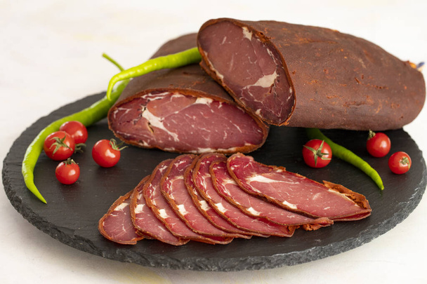 Turkish pastrami on a black stone serving plate. Whole and sliced pastrami. Pastrami is made from the ribeye and beef fillet parts of the cow. local name kayseri pastirma - Photo, Image