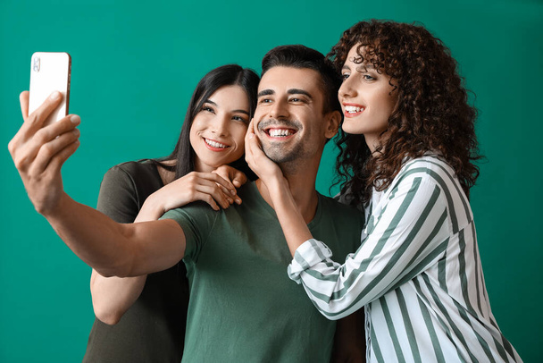 Mies ja kaksi kaunista naista ottavat selfien värin taustalla. Polyamorinen käsite - Valokuva, kuva