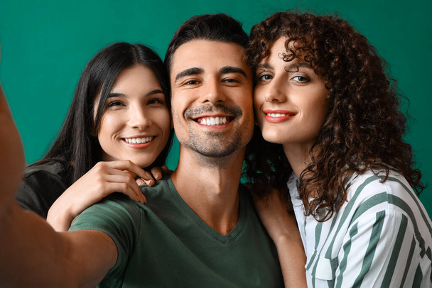 Man and two beautiful women taking selfie on color background. Polyamory concept - Photo, Image