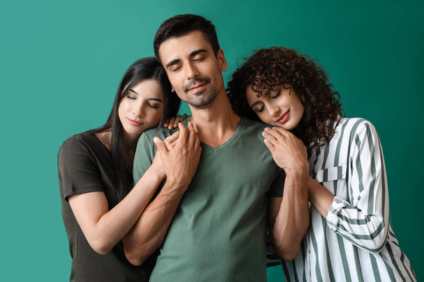Man and two beautiful women on color background. Polyamory concept - 写真・画像