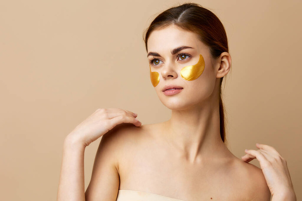 hermosa mujer cuidado de la piel parches para la cara hombros desnudos higiene fondo beige - Foto, Imagen