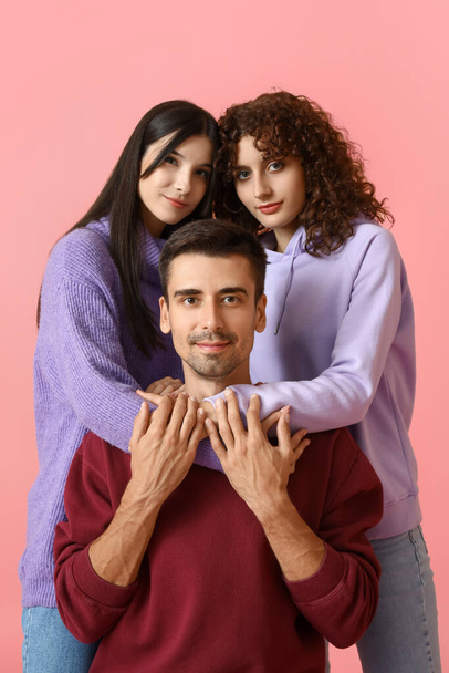 Man and two beautiful women on color background. Polyamory concept - 写真・画像