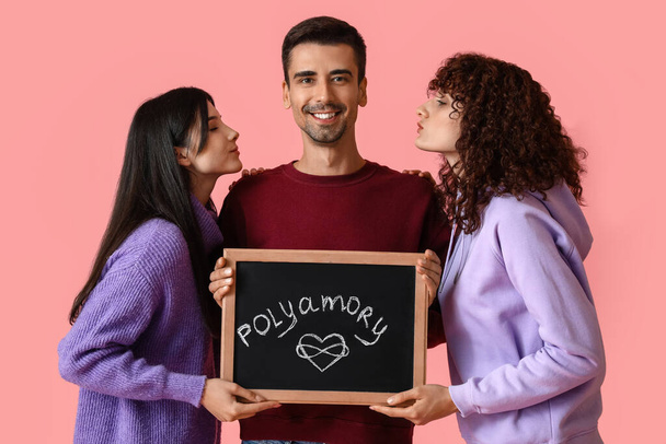 Uomo e due donne che tengono la lavagna con la parola POLIAMORIO sullo sfondo a colori - Foto, immagini