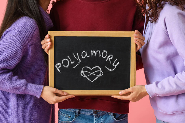 Homme et deux femmes tenant tableau avec mot POLYAMORIE sur fond de couleur - Photo, image