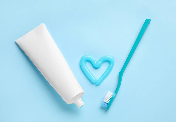 Corazón hecho de pasta de dientes, tubo y cepillo sobre fondo azul - Foto, imagen
