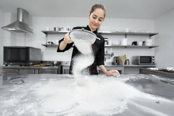 The pastry chef sows the flour through a sieve on the table - Φωτογραφία, εικόνα